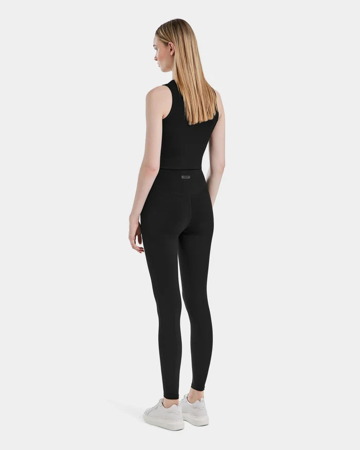 A woman with long, straight blonde hair stands facing away in a sleeveless black top and Rudsak SONOMA - 8525071 Black versatile workout leggings, paired with white sneakers against a plain white background.