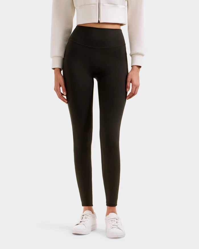 A person wearing high-waisted Rudsak SONOMA - 8525071 Dark Olive leggings, a white cropped jacket, and white sneakers stands against a plain background; only the body from shoulders down is visible.