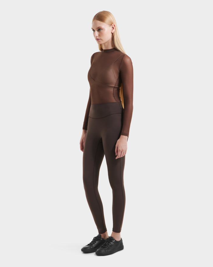 A woman with straight blonde hair wears a sheer brown long-sleeve top, high-waisted Rudsak SONOMA - 8525071 Espresso leggings, and black sneakers, standing against a plain white background.