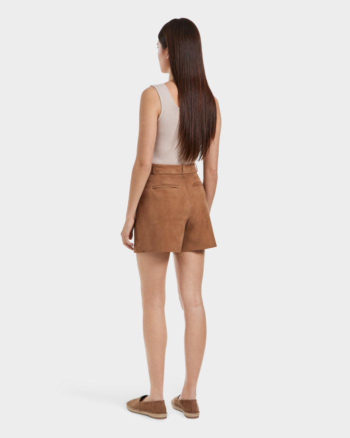 A woman with long brown hair stands facing away against a plain white background, wearing the TERRIE SU - 8525053 Almond tailored suede shorts by Rudsak, a sleeveless beige top, and brown espadrille shoes.