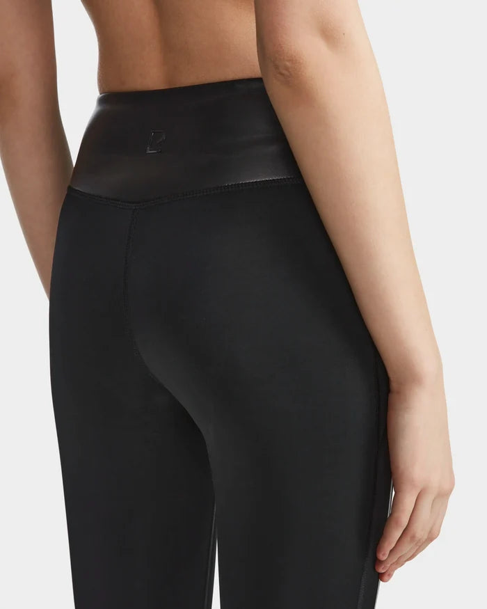 A person is shown from the back wearing Rudsak THEA - 8523003 BLACK high-waisted leggings with a shiny waistband, one arm relaxed at their side, against a plain white background.