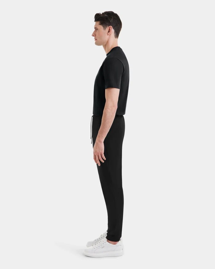 A man stands in profile facing left, wearing the TUSTIN - 6525029 Black jogger pants by Rudsak, a black t-shirt, and white sneakers against a plain light gray background.
