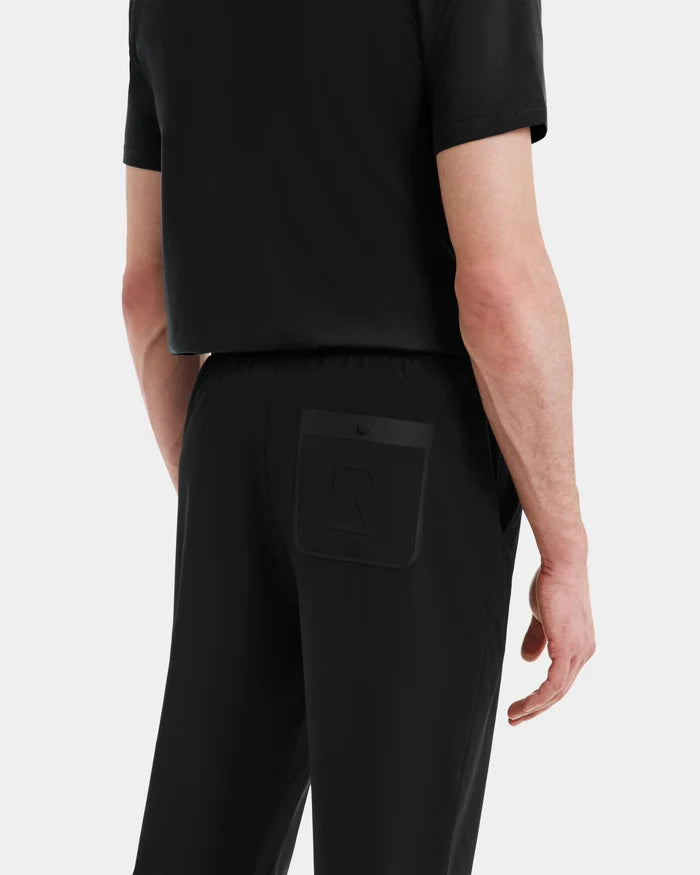 A man in mens casual wear, seen from the back, wears a black short-sleeve shirt and Rudsak TUSTIN - 6525029 Black jogger pants, which feature technical fabric and a flap pocket with a raised R design on the right side.