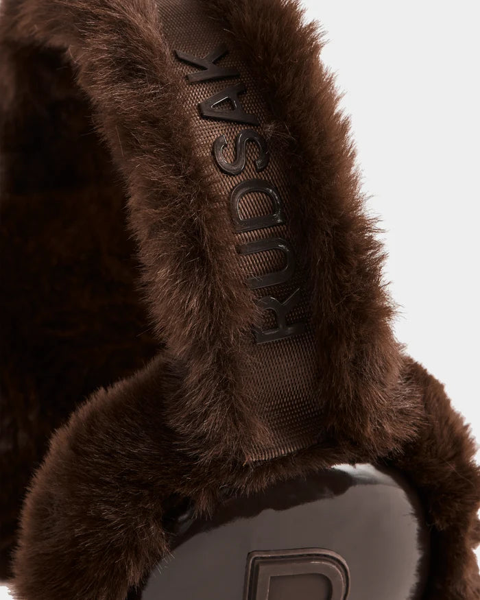 Close-up of VALENCIA - 8425543 Espresso faux fur earmuffs by Rudsak, featuring an embroidered headband and glossy black ear covers with a raised R logo—a chic winter accessory.