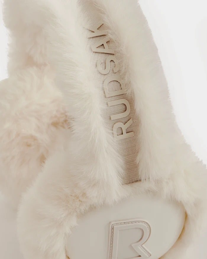 Close-up of the Rudsak VALENCIA - 8425543 Vanilla earmuffs featuring white, fluffy faux fur, an embroidered Rudsak band, and a raised "R" logo—an essential winter accessory.