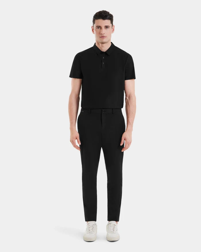 A man stands facing forward in the Rudsak VERNON - 6525025 Black short-sleeve polo shirt, paired with tapered-leg trousers and white sneakers against a plain white background—effortless modern style.