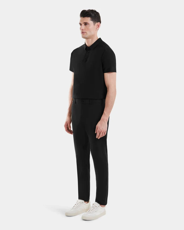 A man models the Rudsak VERNON - 6525025 Black polo against a white background, paired with tapered trousers and white sneakers for a clean, modern look.