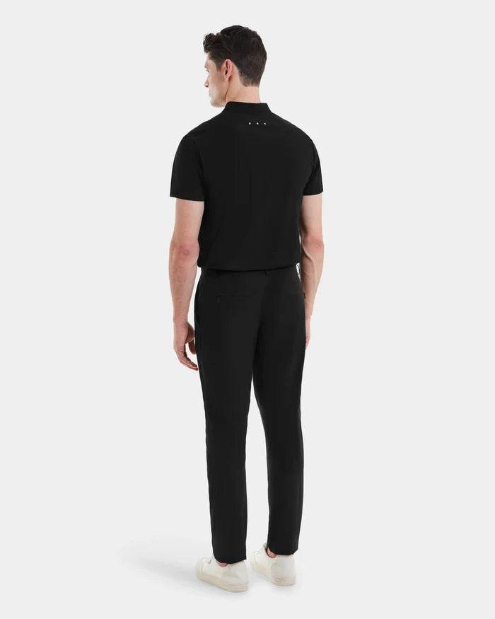 A man faces away, wearing Rudsaks VERNON - 6525025 Black short-sleeve polo and tapered trousers with white sneakers, set against a plain white background—a minimalist look for the modern wardrobe.