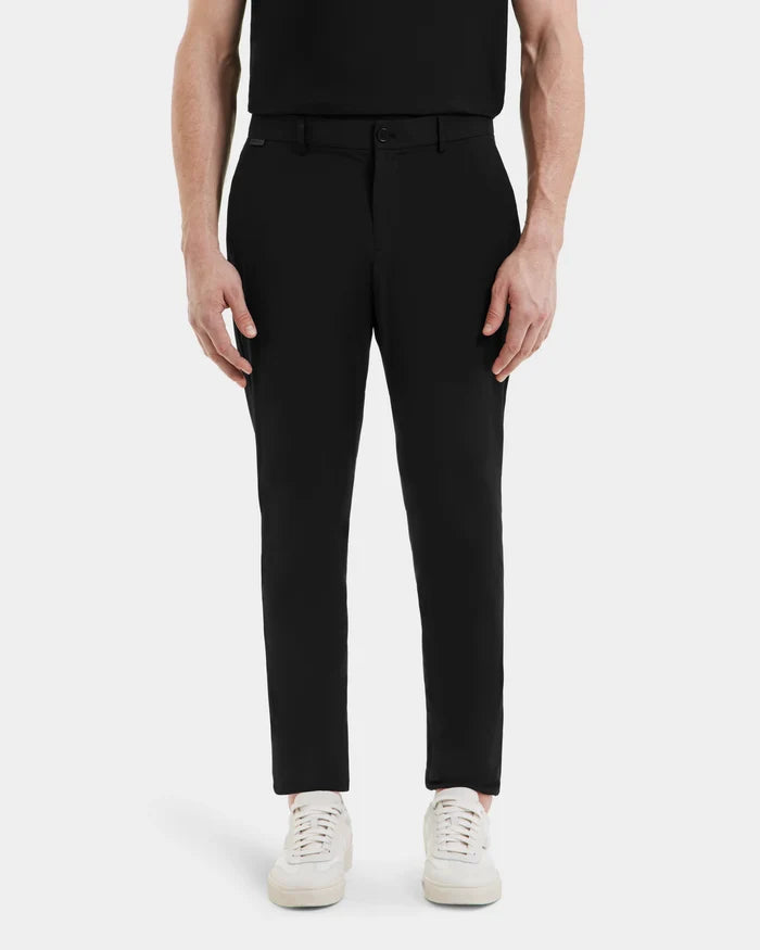 Wearing the VERNON - 6525025 Black trousers by Rudsak and white sneakers, a person stands with arms relaxed at their sides in a black top, set against a plain white background—a sleek choice for any modern wardrobe.