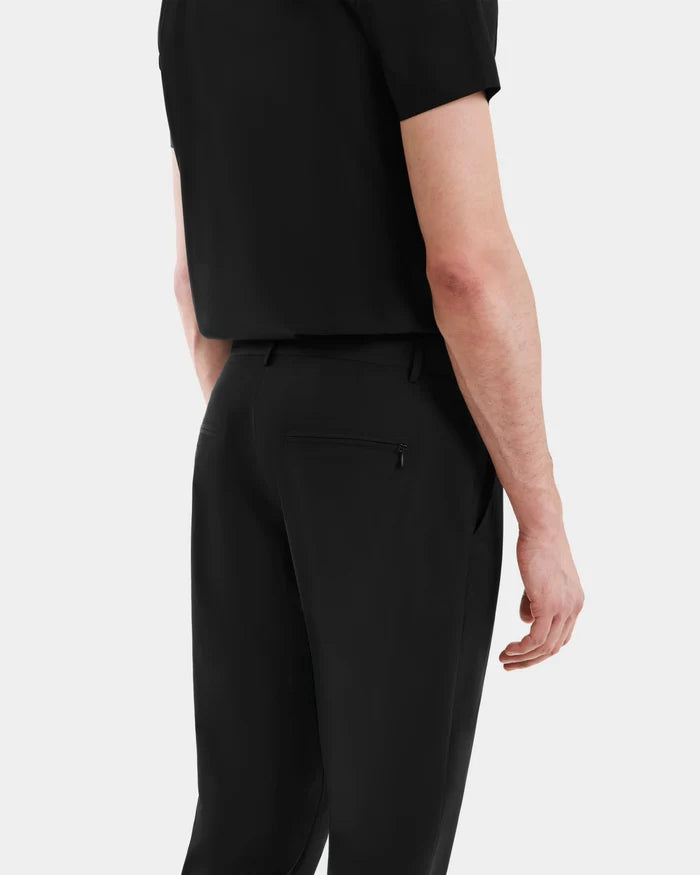 A person is seen from the back wearing Rudsak’s VERNON - 6525025 Black short-sleeve shirt and tapered-leg trousers, their right arm relaxed by their side against a plain light background—a modern wardrobe essential.