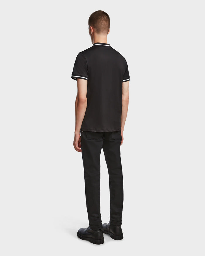 A person with short hair, facing away, is wearing the Rudsak VICK - M523004 Black mens polo—tailored fit with white stripes on sleeves and collar—paired with black pants and shoes against a plain white background.