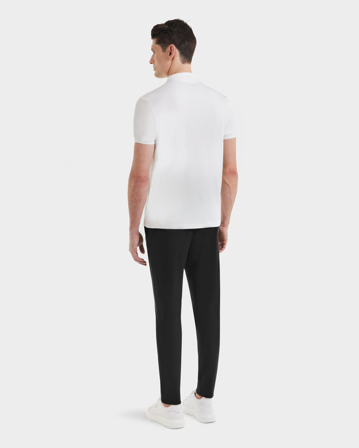 A man, with his back to the camera, models the Rudsak VICK - M523004 Optic White men’s polo shirt, styled with black pants and white sneakers against a plain white background.