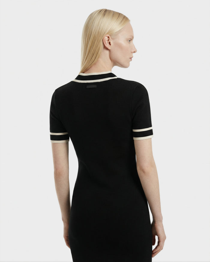 A woman with straight blonde hair is seen from behind wearing the Rudsak VINNIE - 8526038 Black fitted knit midi dress, featuring white trim on the sleeves and collar, against a plain light background.