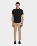 A man faces forward against a white background, wearing Rudsaks WELLS - 6525017 black short-sleeve polo shirt in lightweight technical fabric, paired with beige slim-fit pants and black shoes.