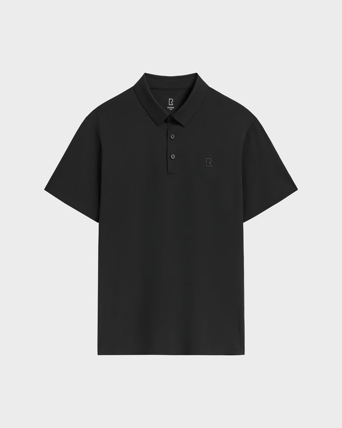 The WELLS - 6525017 Black by Rudsak is a tailored-fit polo with short sleeves, classic collar, three buttons, and an embroidered R logo on the chest, all in lightweight technical fabric. Shown on a light gray background.