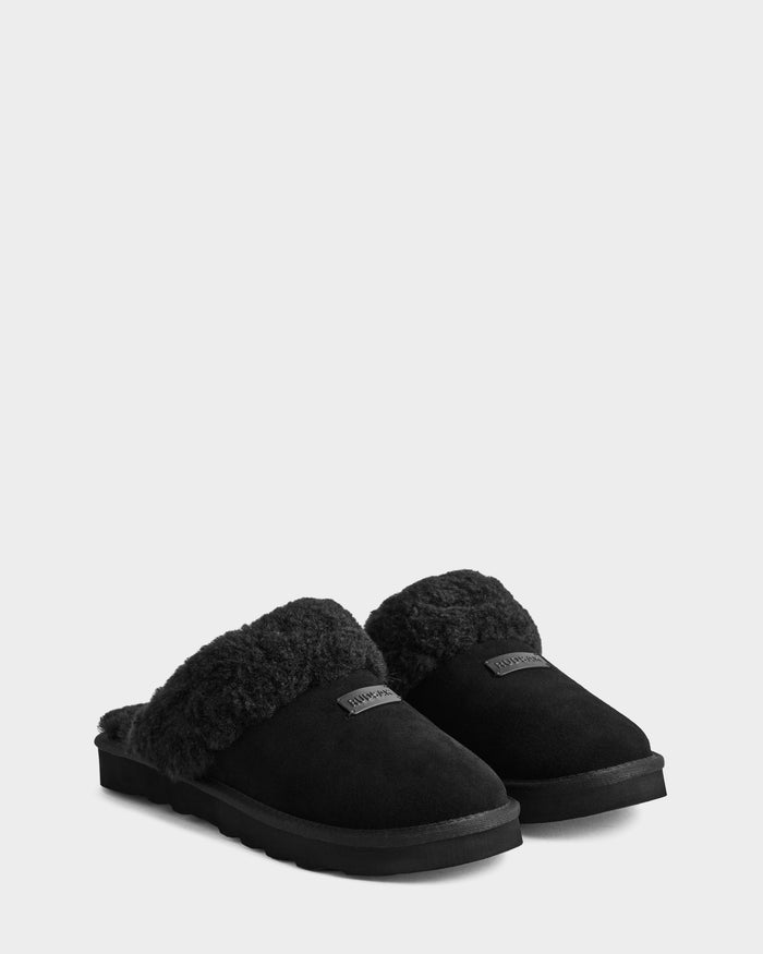 A pair of WILBER - 6225509 Black men’s slippers by Rudsak, featuring fluffy faux shearling uppers and textured soles with a visible logo patch, are placed side by side on a plain light background.