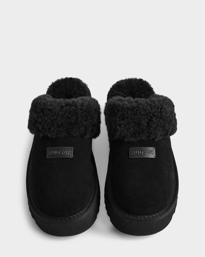A pair of WILMA - 8225582 Black suede slipper slip-ons by Rudsak, with thick faux fur lining and fold-over cuffs, are shown side by side on a white background. The women’s slippers feature a front label reading RUDSAK—perfect for winter.