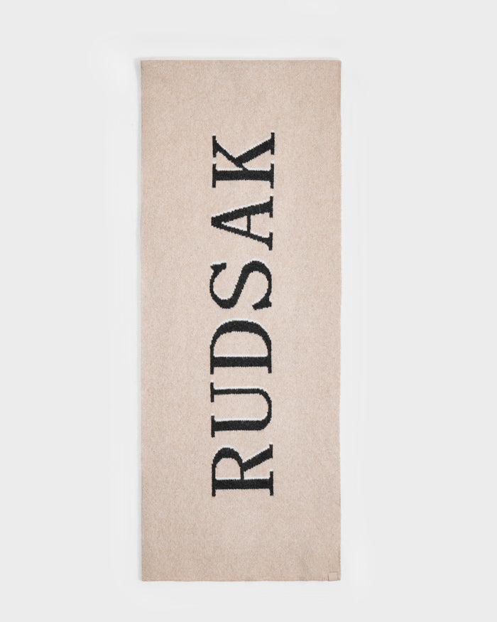 The Rudsak WYATT - 6425039 Vanilla is a beige rectangular towel featuring "RUDSAK" in bold black letters down the center—a stylish winter essential. The towel is showcased on a plain white background.