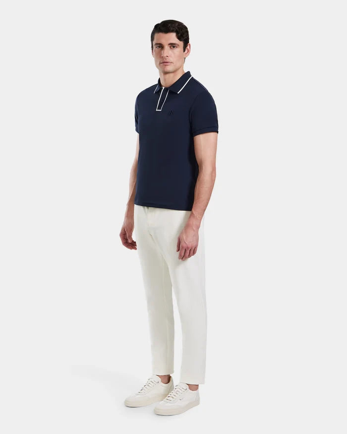 A man stands against a plain background, wearing the Rudsak XAVIER - 6524027 polo shirt in navy with white trim, paired with white pants and sneakers.
