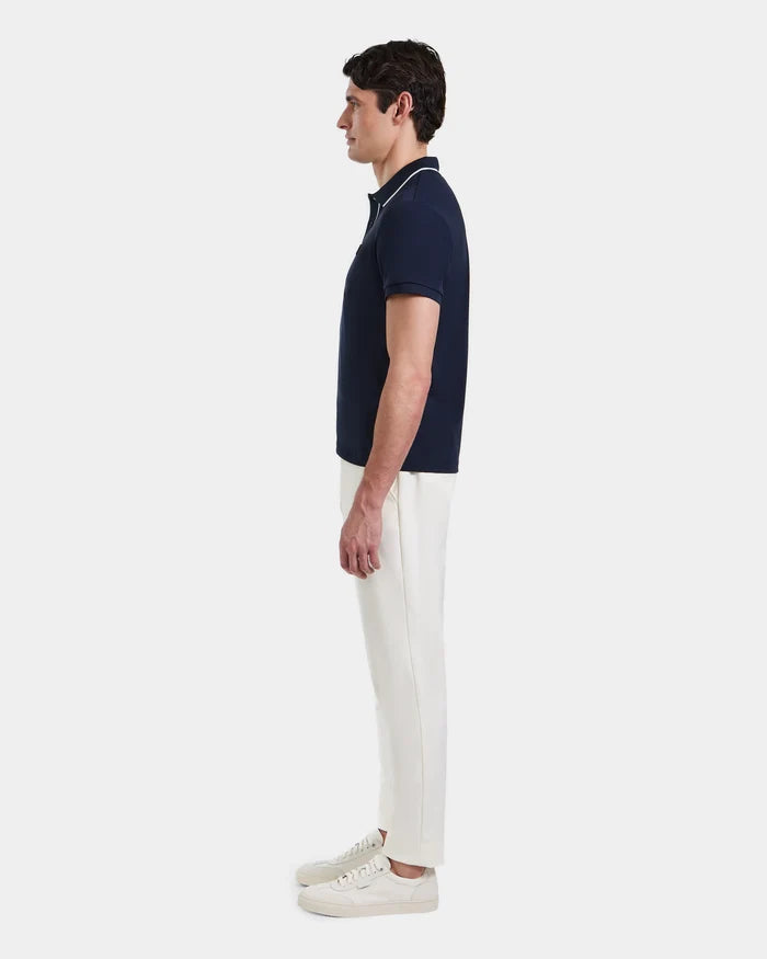 A man stands in profile against a plain background, wearing the Rudsak XAVIER - 6524027 Navy polo shirt, paired with white pants and white sneakers.