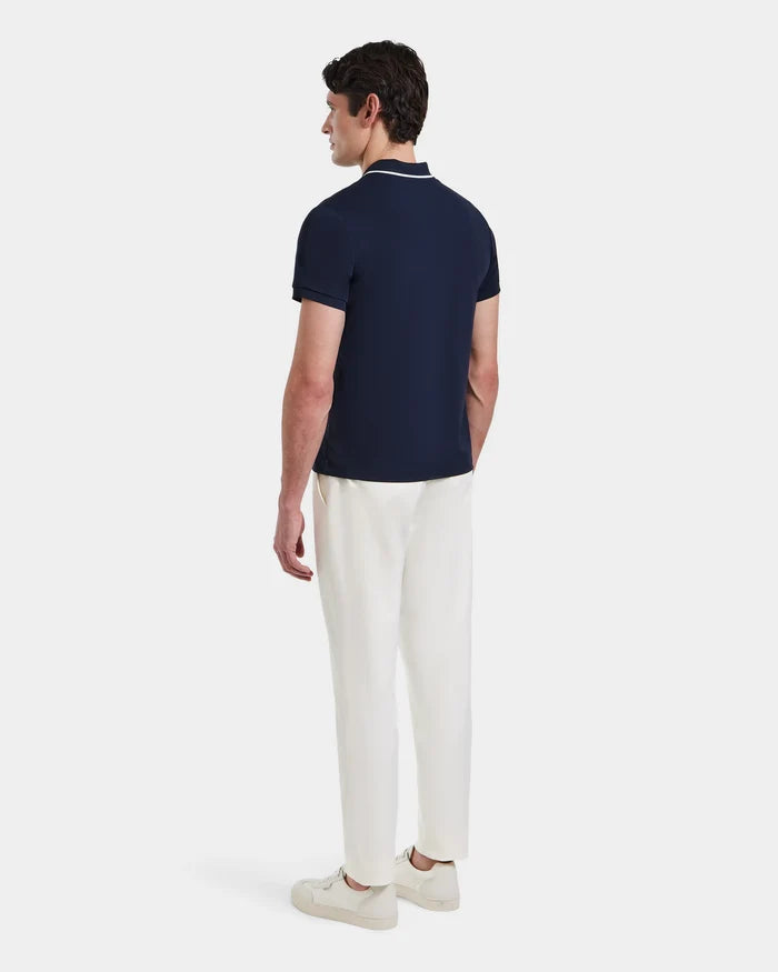 A man stands facing away, wearing the XAVIER - 6524027 Navy polo shirt by Rudsak with white pants and sneakers, set against a plain white background.