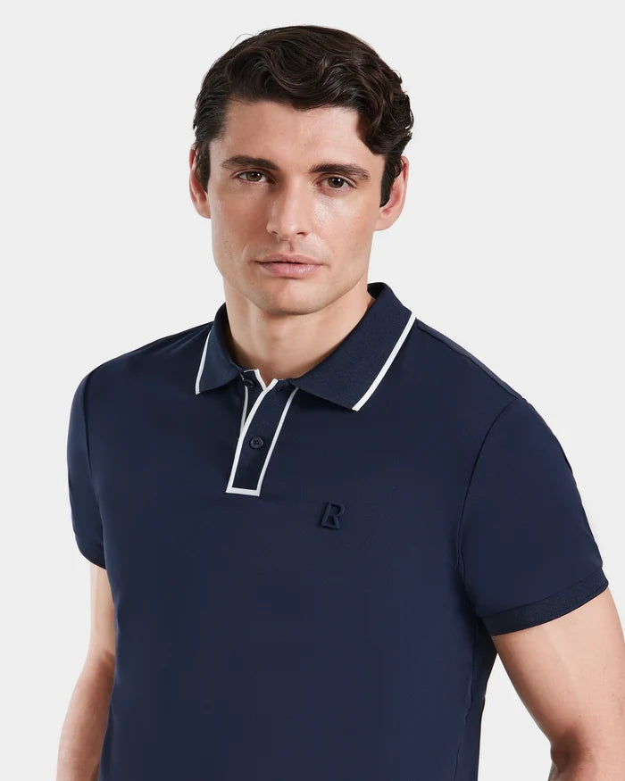 A man with short brown hair wears the Rudsak XAVIER - 6524027 mens polo in navy, featuring white collar trim and a small R logo on the chest, standing against a plain white background.